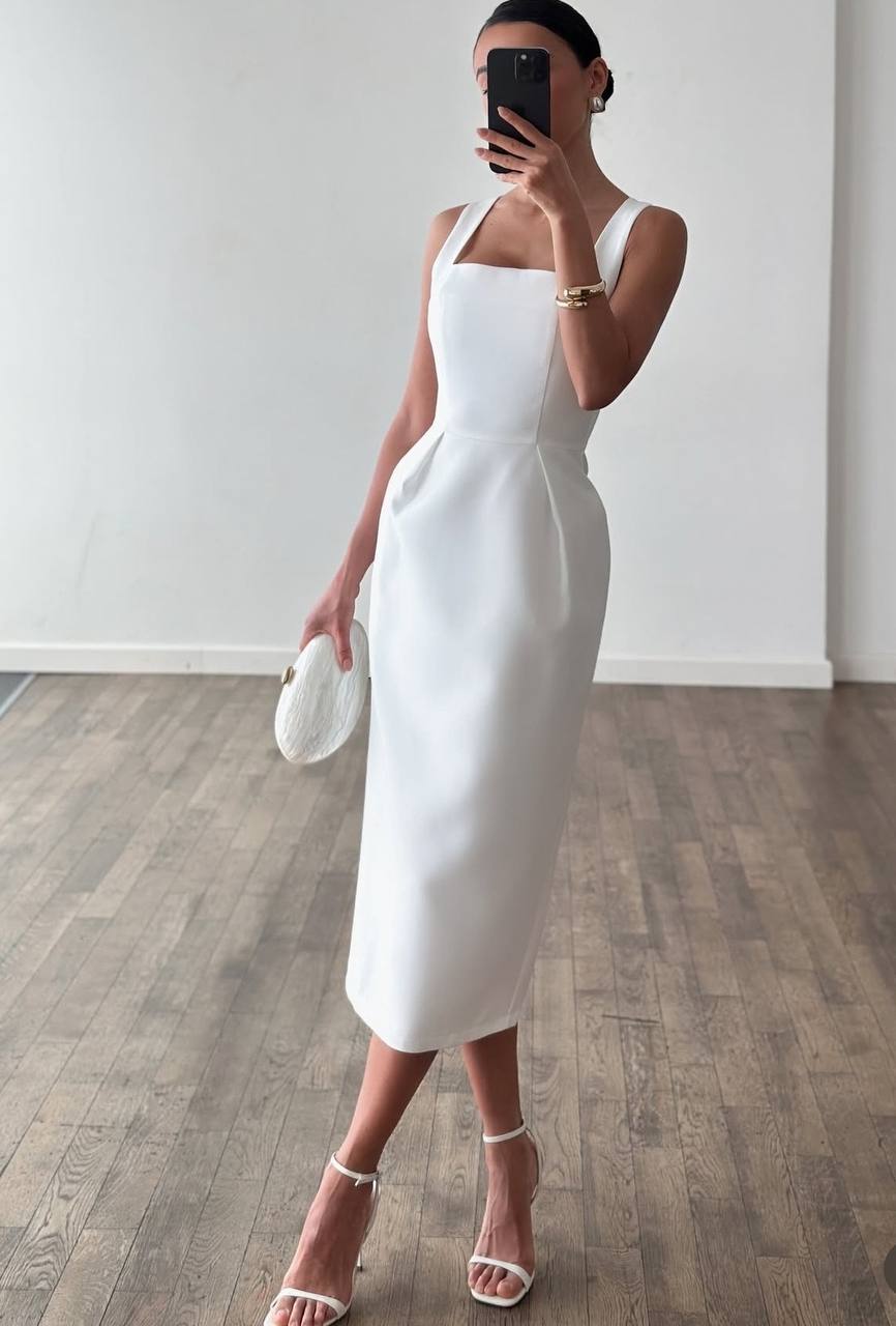 Woman in a white dress standing on a wooden floor with a plain white wall background