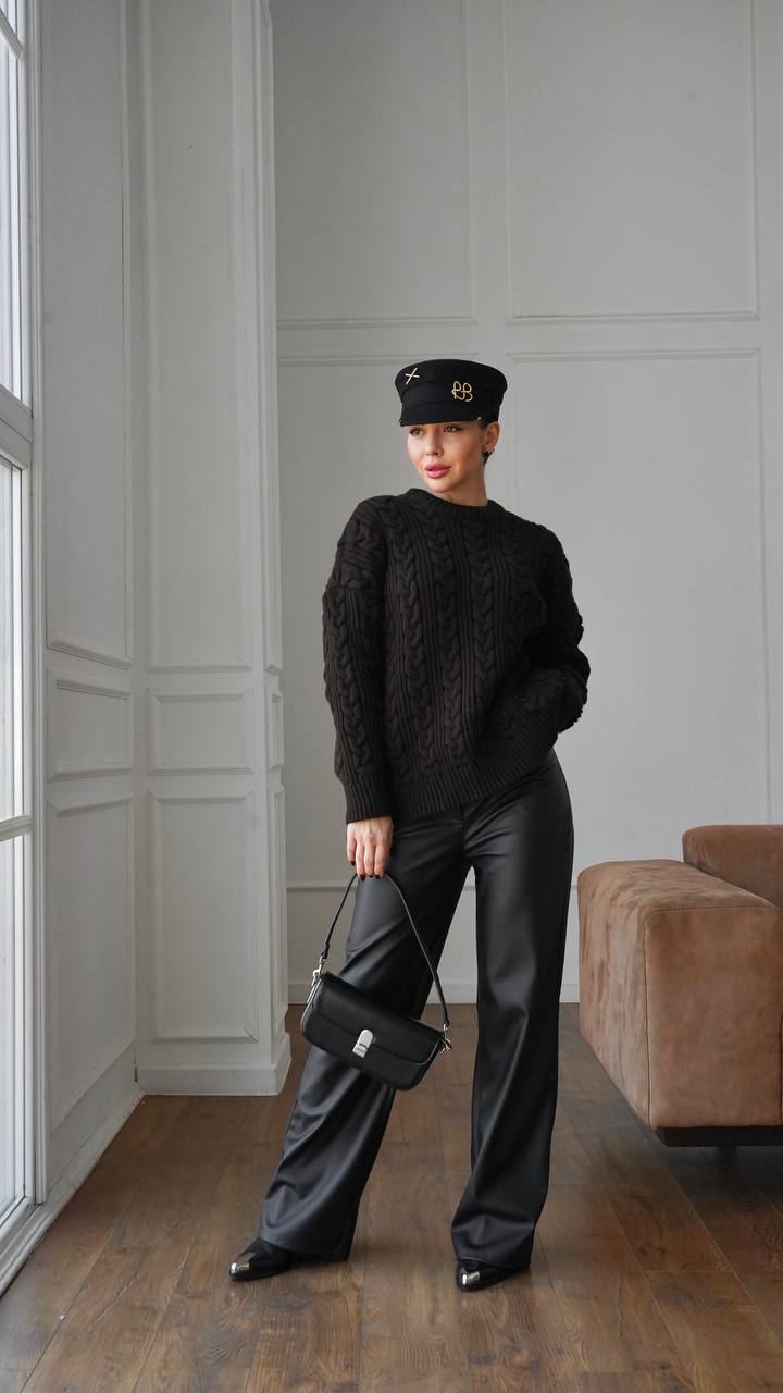Person wearing a black sweater and pants in a room with a window and sofa.