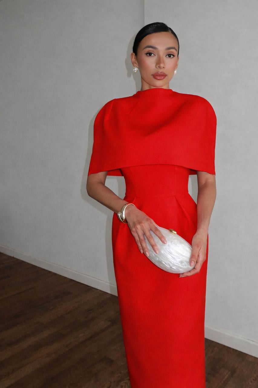 Woman in a red dress holding a white clutch against a plain background