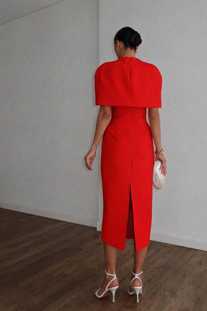 Person wearing a red dress with a slit, standing against a plain wall.