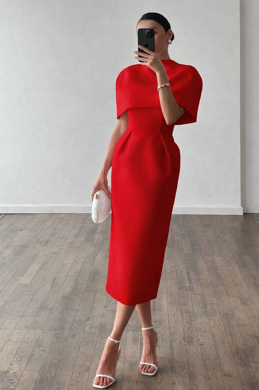 Person wearing a red dress holding a white clutch in a room with wooden flooring.