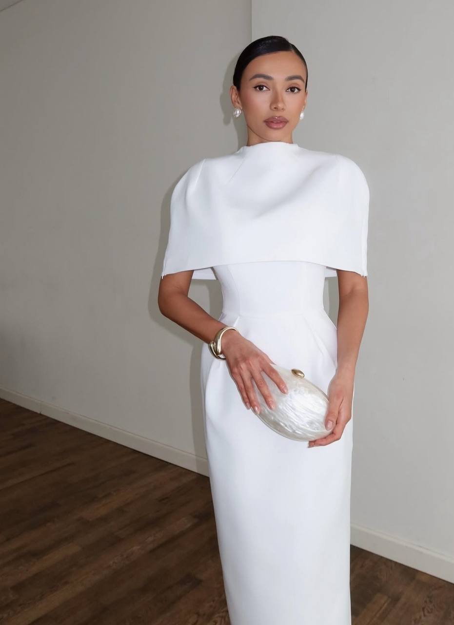 Woman in a white dress holding a clutch against a plain background