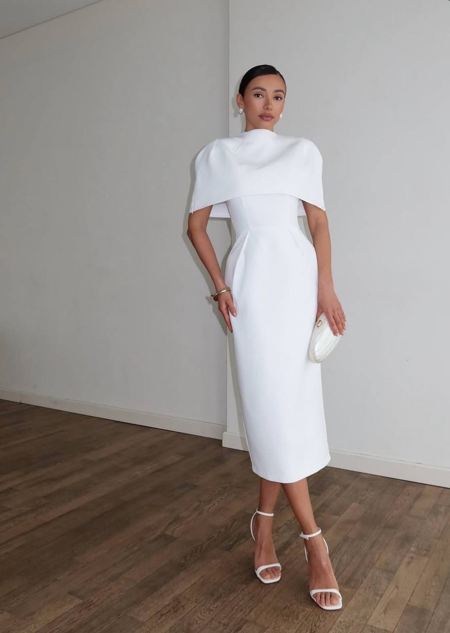Woman in a white dress standing against a plain wall.