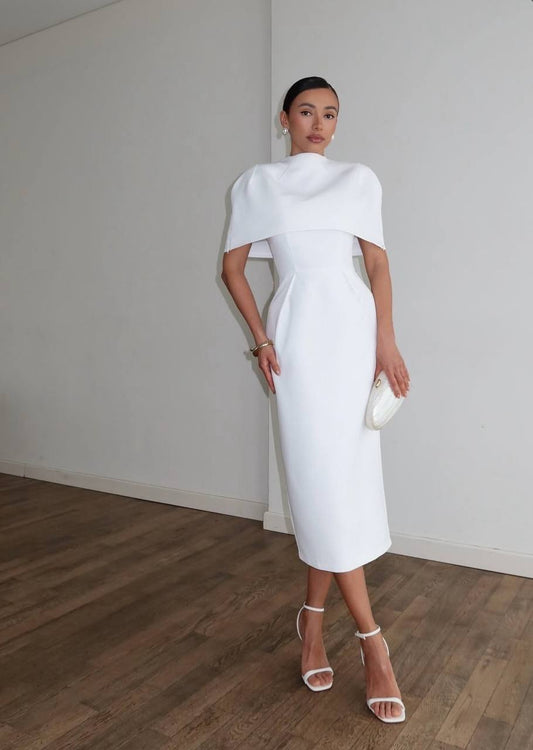Woman in a white dress standing against a plain wall.