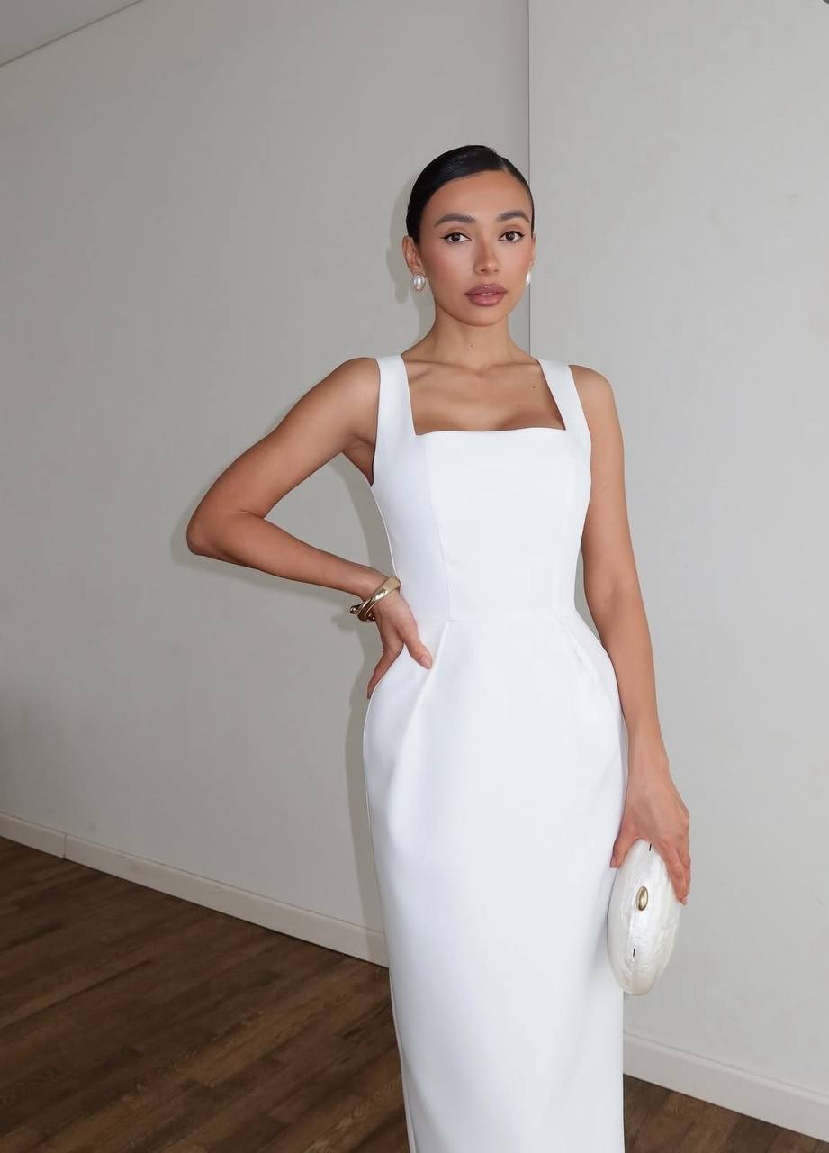 Woman in a white dress holding a clutch against a plain background