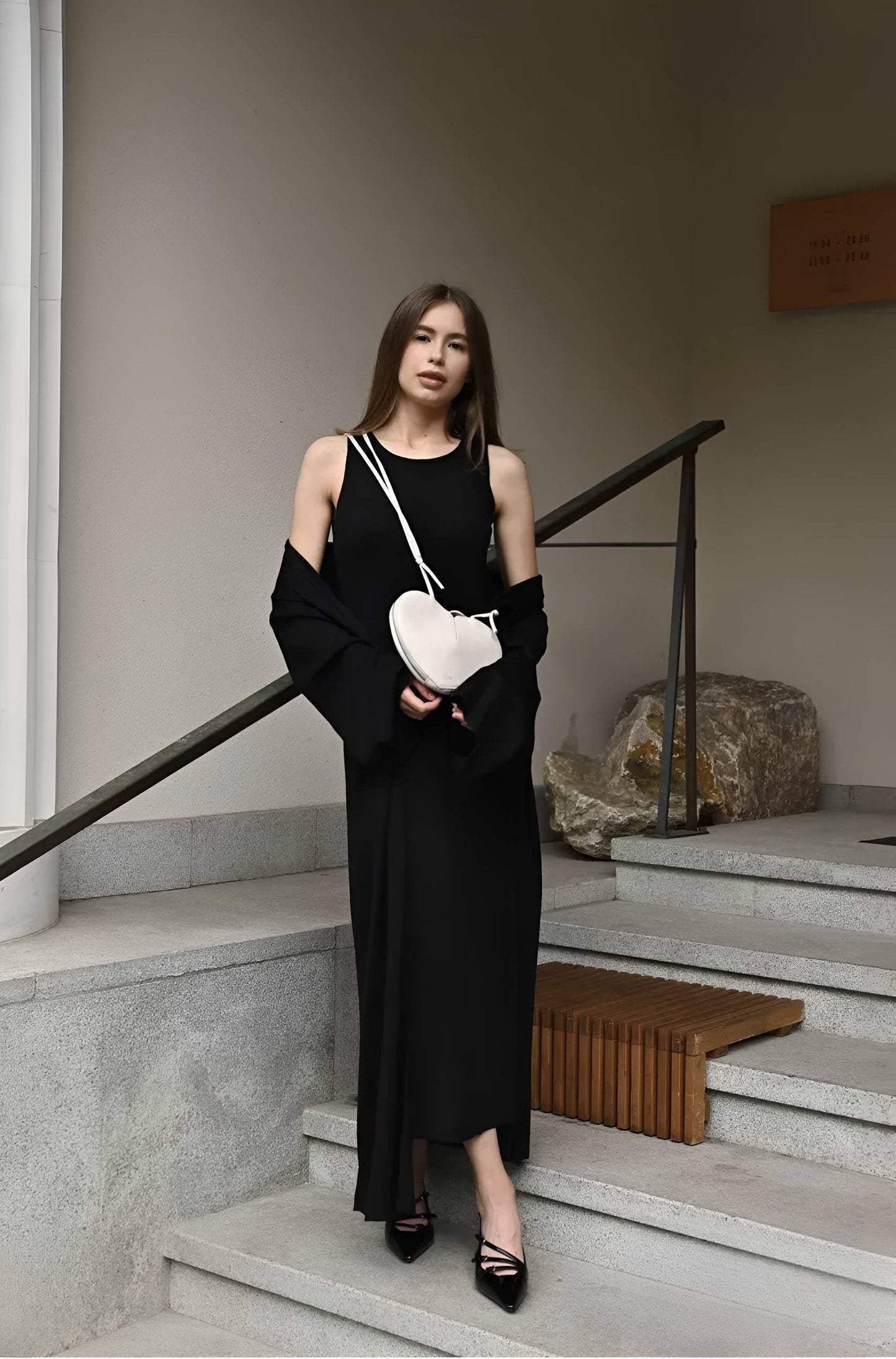 Woman in a black dress holding a white clutch on stone steps.