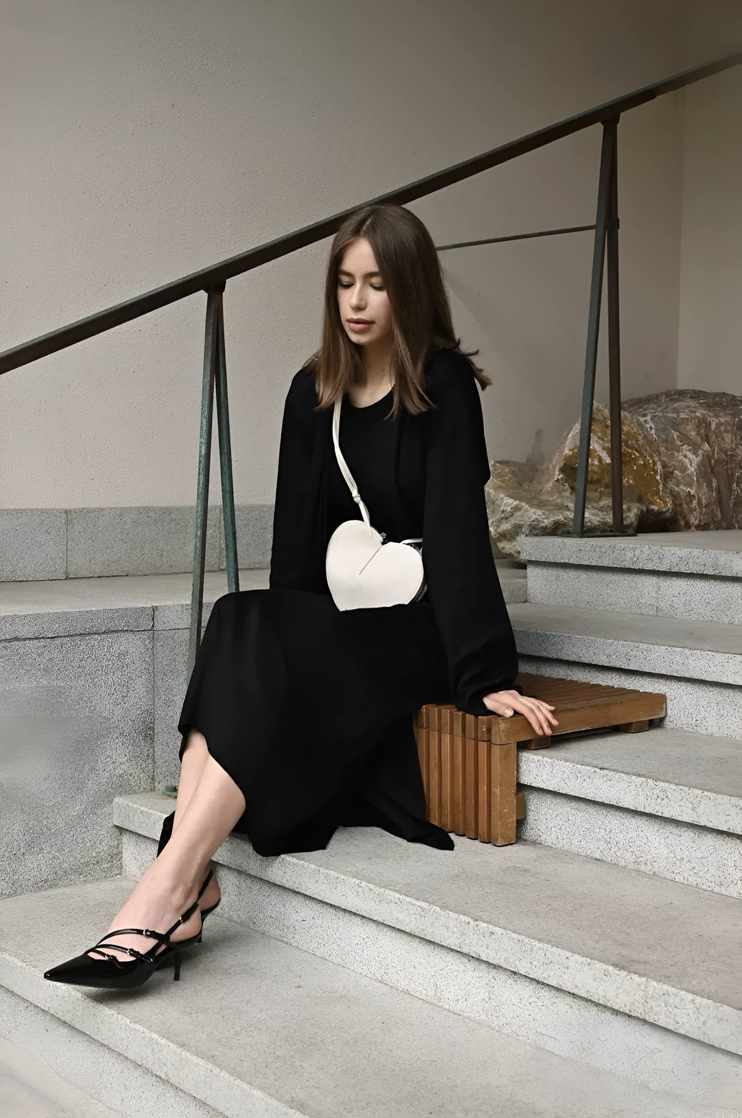 Woman in a black dress sitting on stairs holding a white handbag