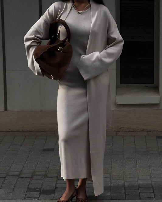 Person wearing a long white coat and holding a brown bag on a street.