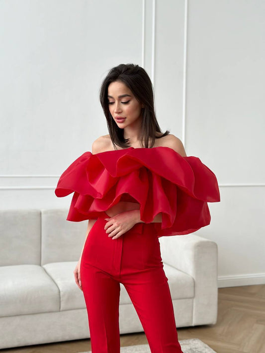 Woman wearing a red outfit with ruffled top in a room with a white couch.