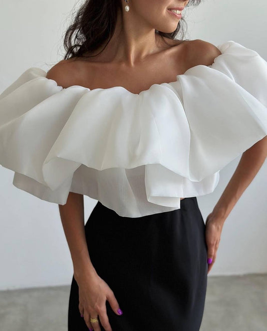 Woman wearing a white off-shoulder top with ruffled sleeves against a plain background