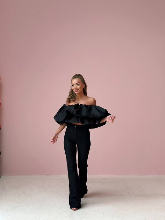 Woman wearing a black off-shoulder top and black pants against a pink background