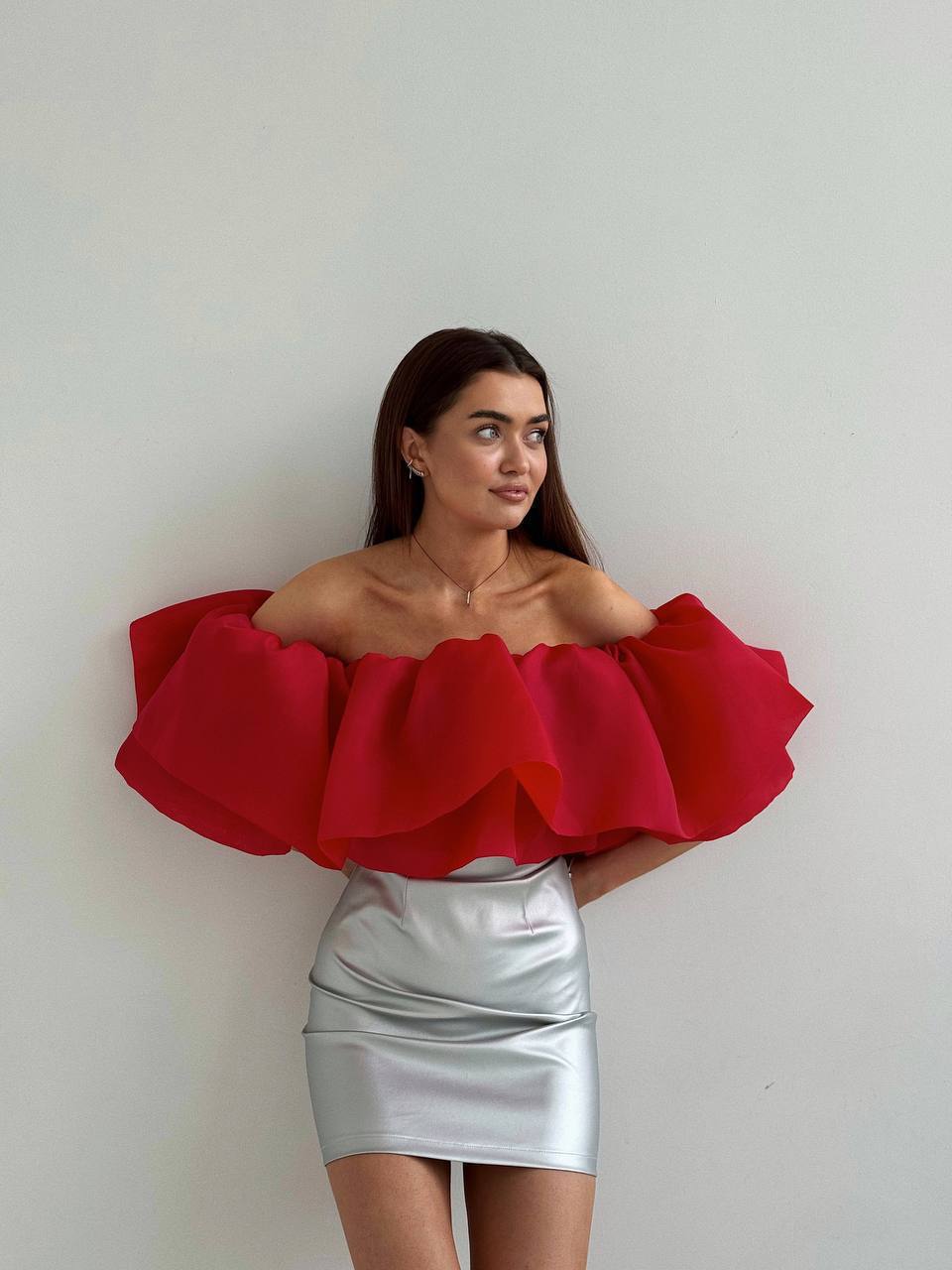 Woman wearing a red off-shoulder top and silver skirt against a plain background