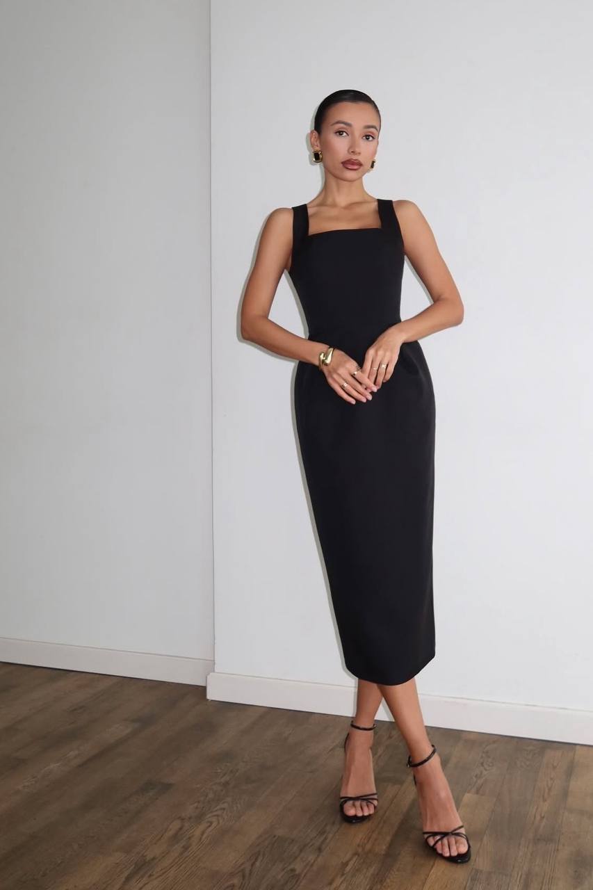 Woman wearing a black dress standing against a white wall.