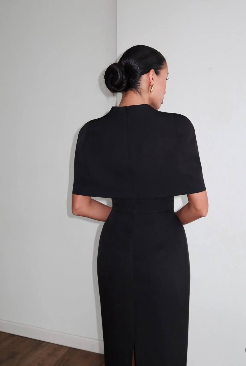 Woman wearing a black dress with a cape against a white wall