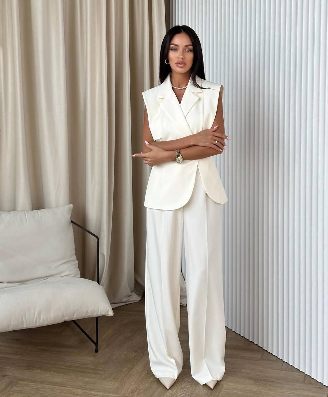 Woman in a white suit standing in a modern room with neutral decor.