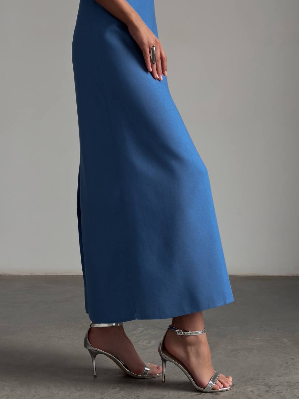 Person wearing a blue skirt with silver high-heeled shoes on a neutral background