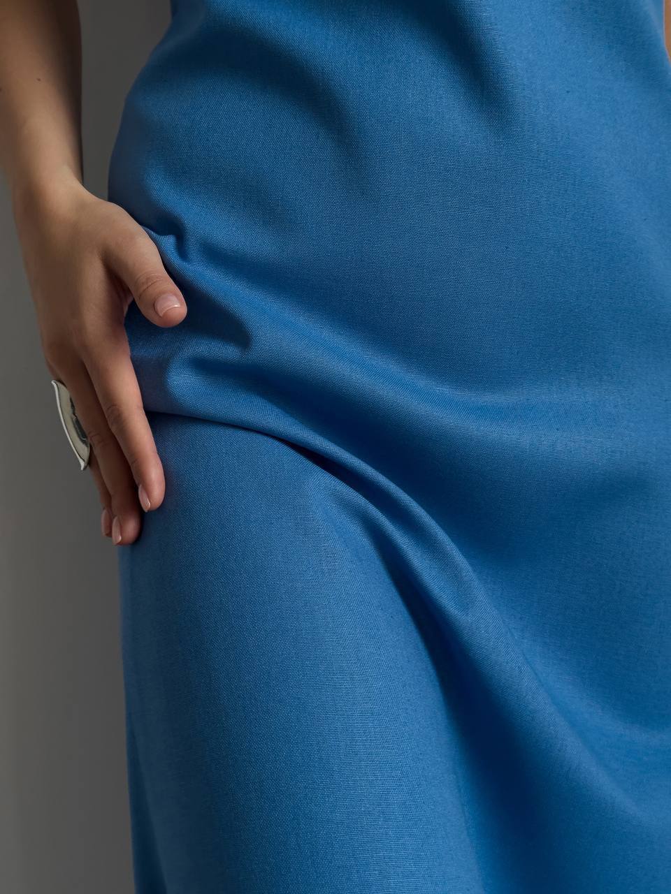 Close-up of a blue fabric with a hand touching it, on a gray background