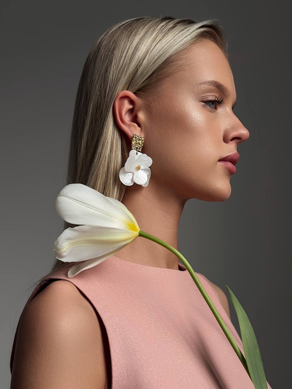 Woman wearing white floral earrings with a tulip against a gray background