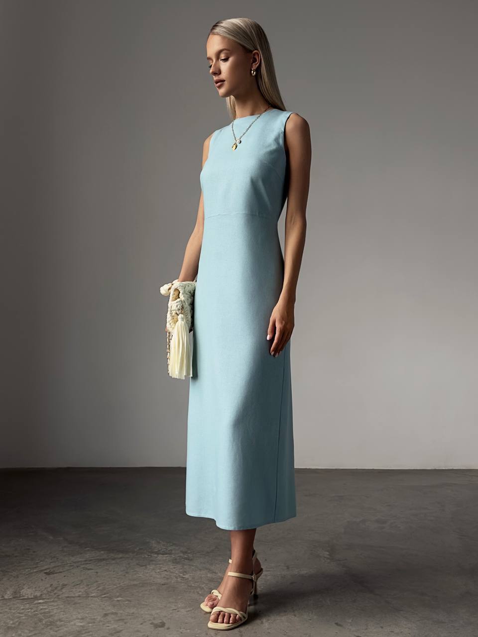 Woman wearing a light blue dress holding a clutch against a gray background
