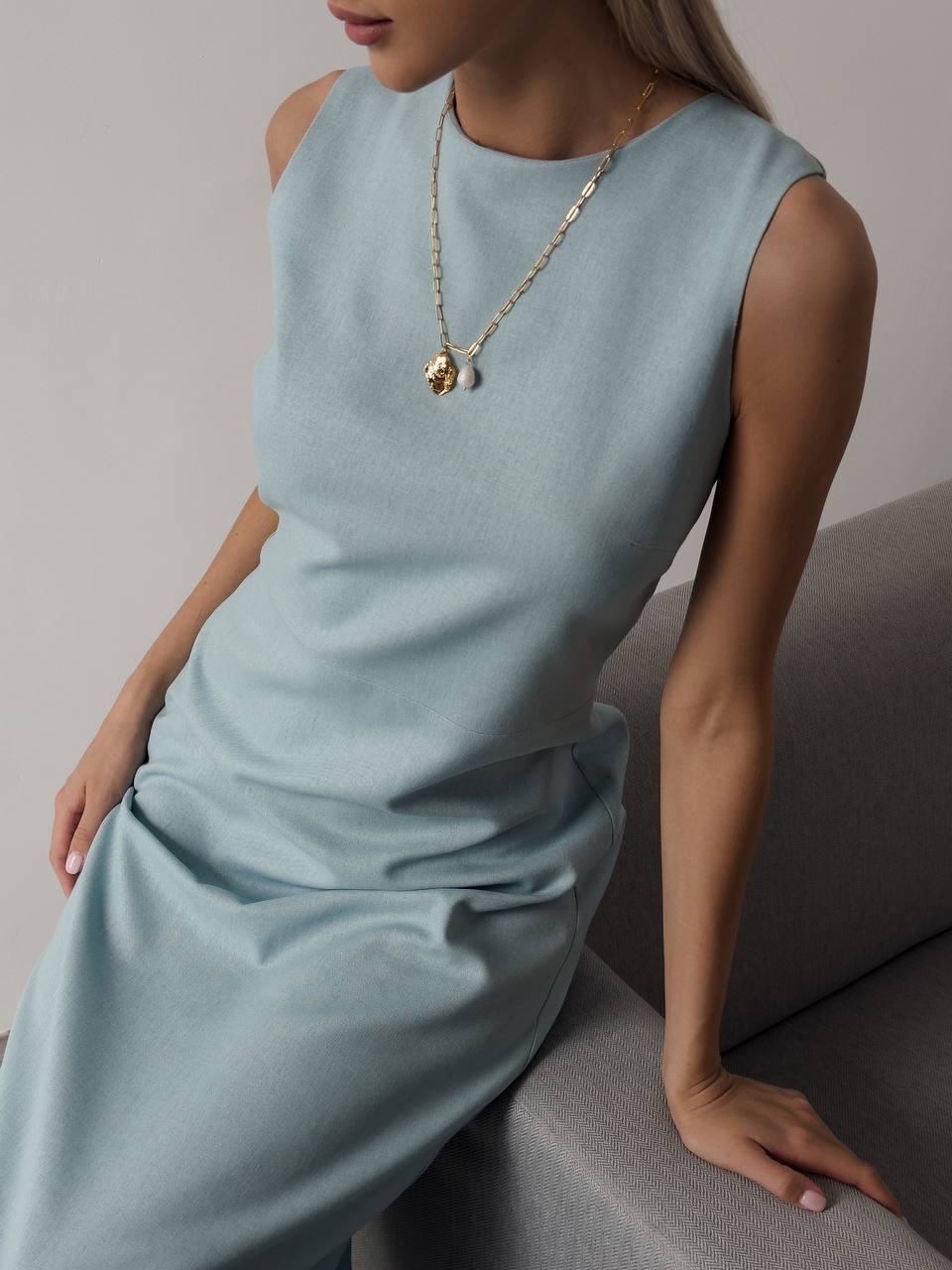 Woman wearing a light blue dress with a gold necklace against a neutral background