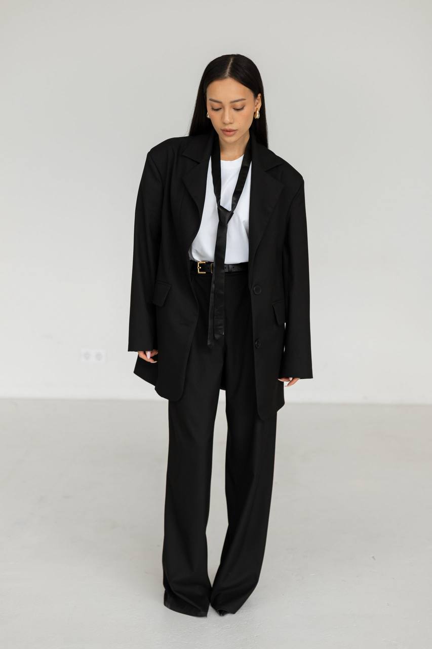 Person wearing a black coat and pants with a white shirt underneath on a plain background