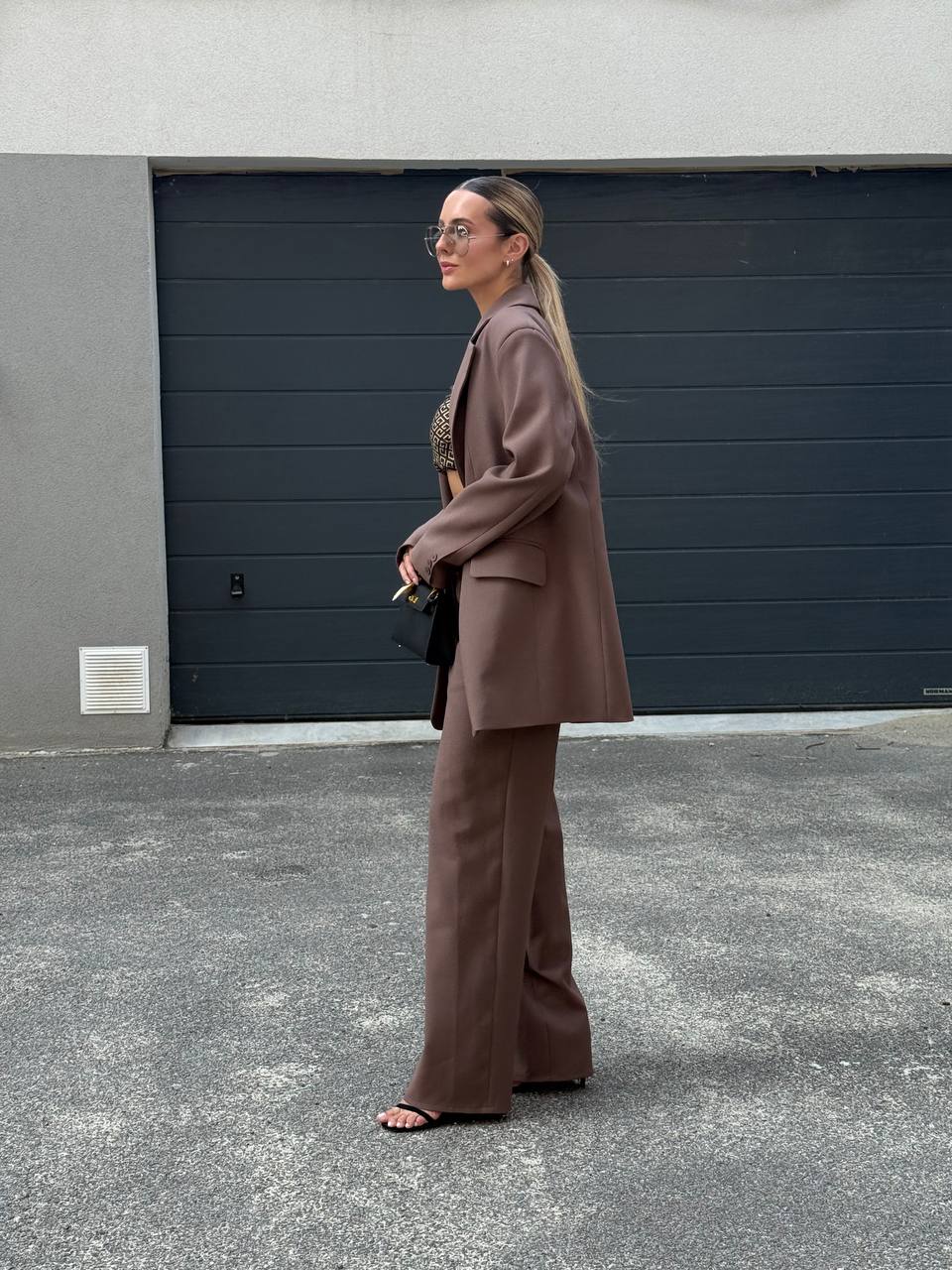 Woman in a brown suit standing in front of a gray wall.