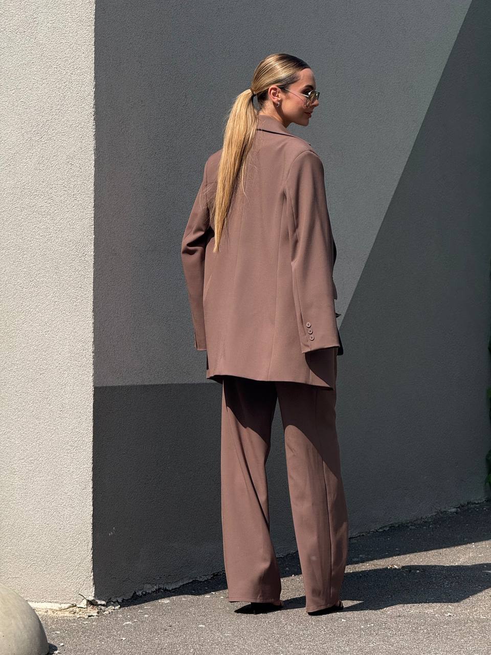Person wearing a brown outfit standing against a gray wall.