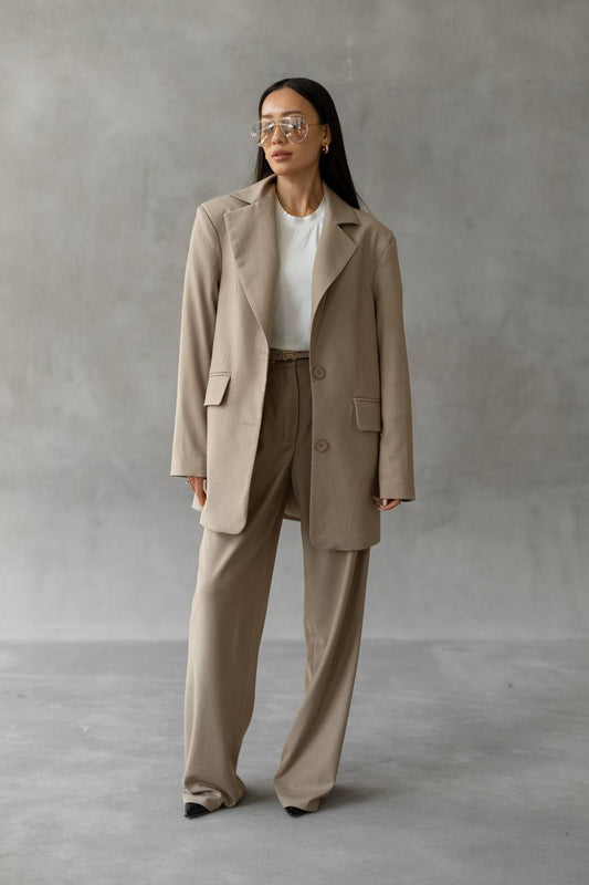 Woman wearing a beige suit standing against a plain background