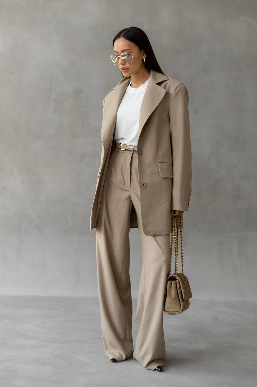Woman in a beige suit with a white shirt, standing against a plain background