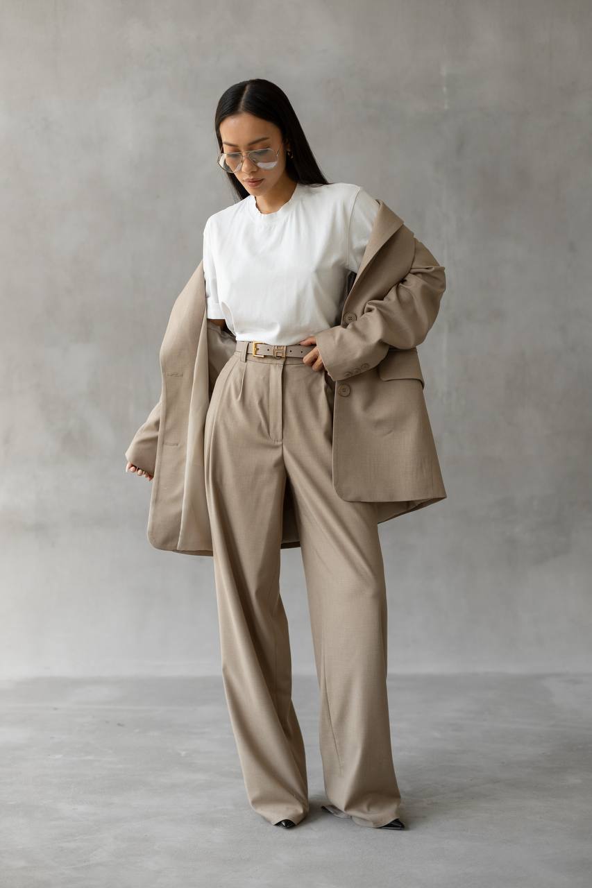 Woman wearing a beige suit and white shirt against a gray background