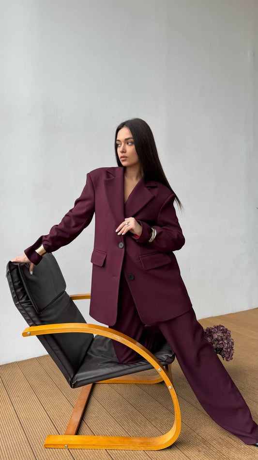 Woman in a burgundy suit sitting on a modern chair against a plain background