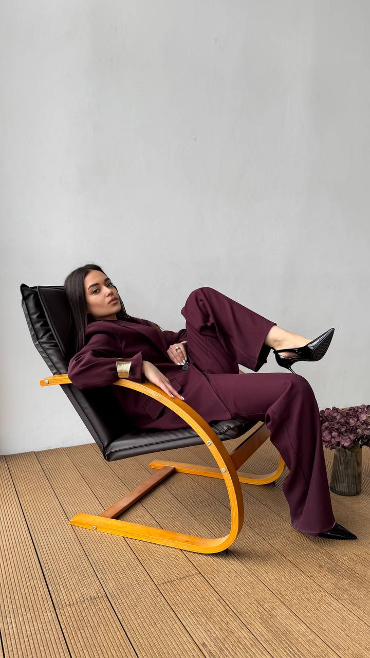 Woman in a purple outfit sitting on a modern black and yellow chair against a plain wall.