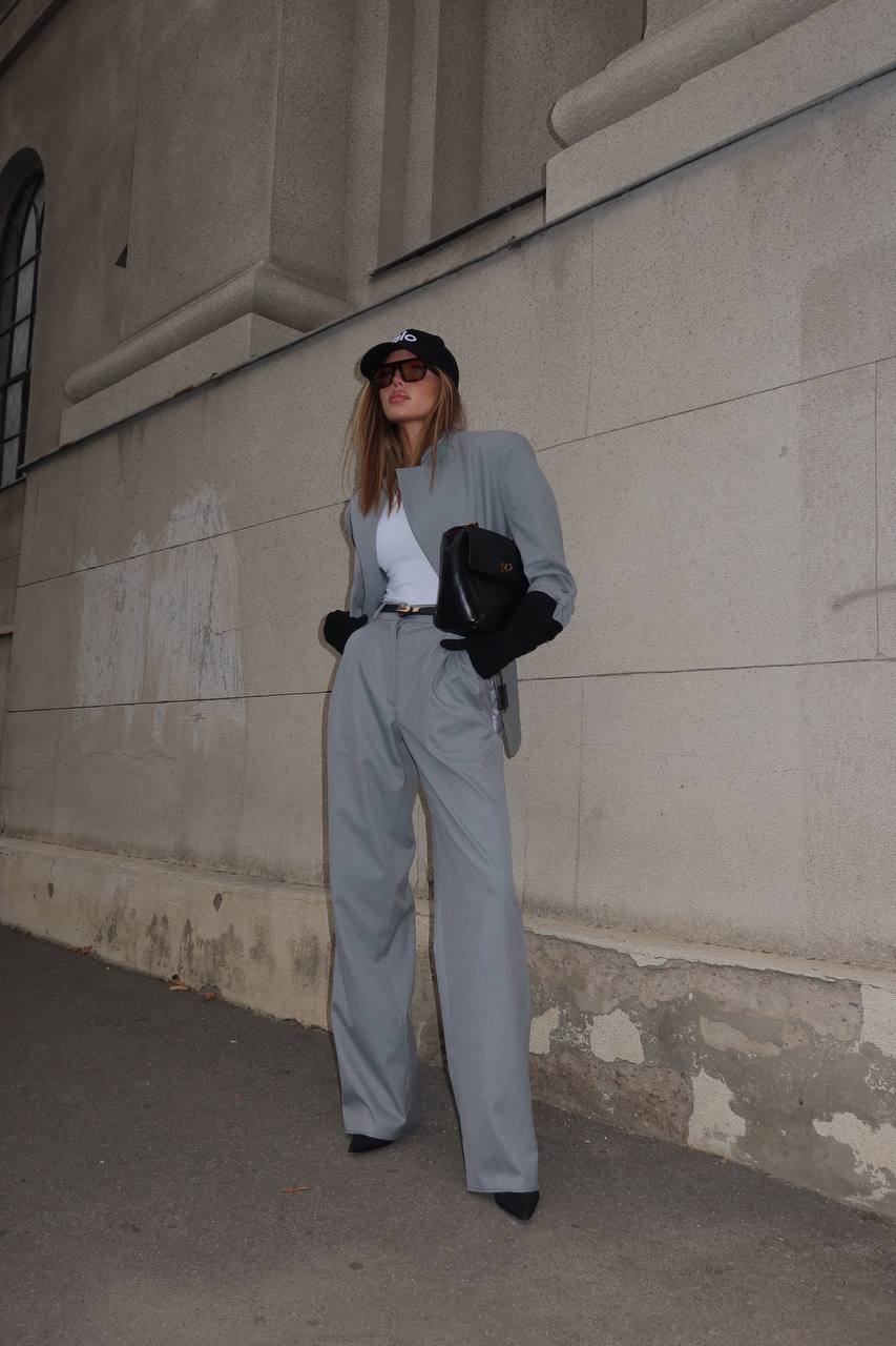 Woman in gray suit standing against a beige wall