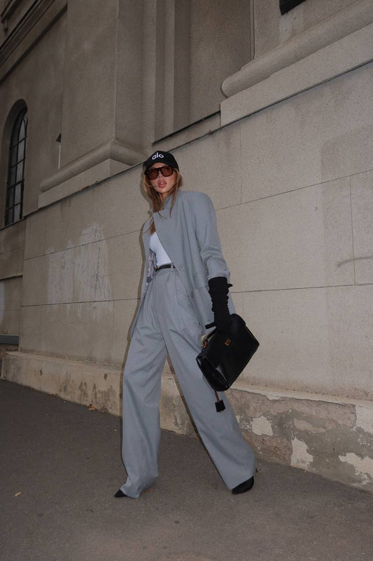 Person in gray outfit standing against a beige building wall