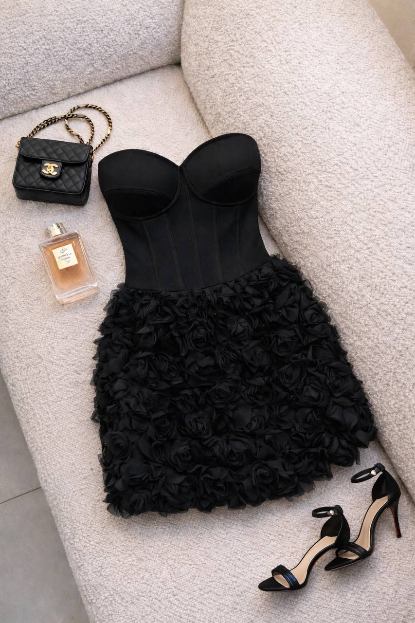 Black strapless dress with floral details, black handbag, perfume bottle, and high heels on a light gray surface.