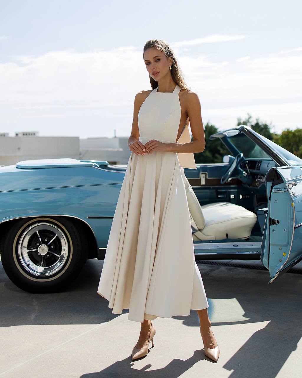Woman in a white dress standing next to a vintage blue car. Wedding Guest dress