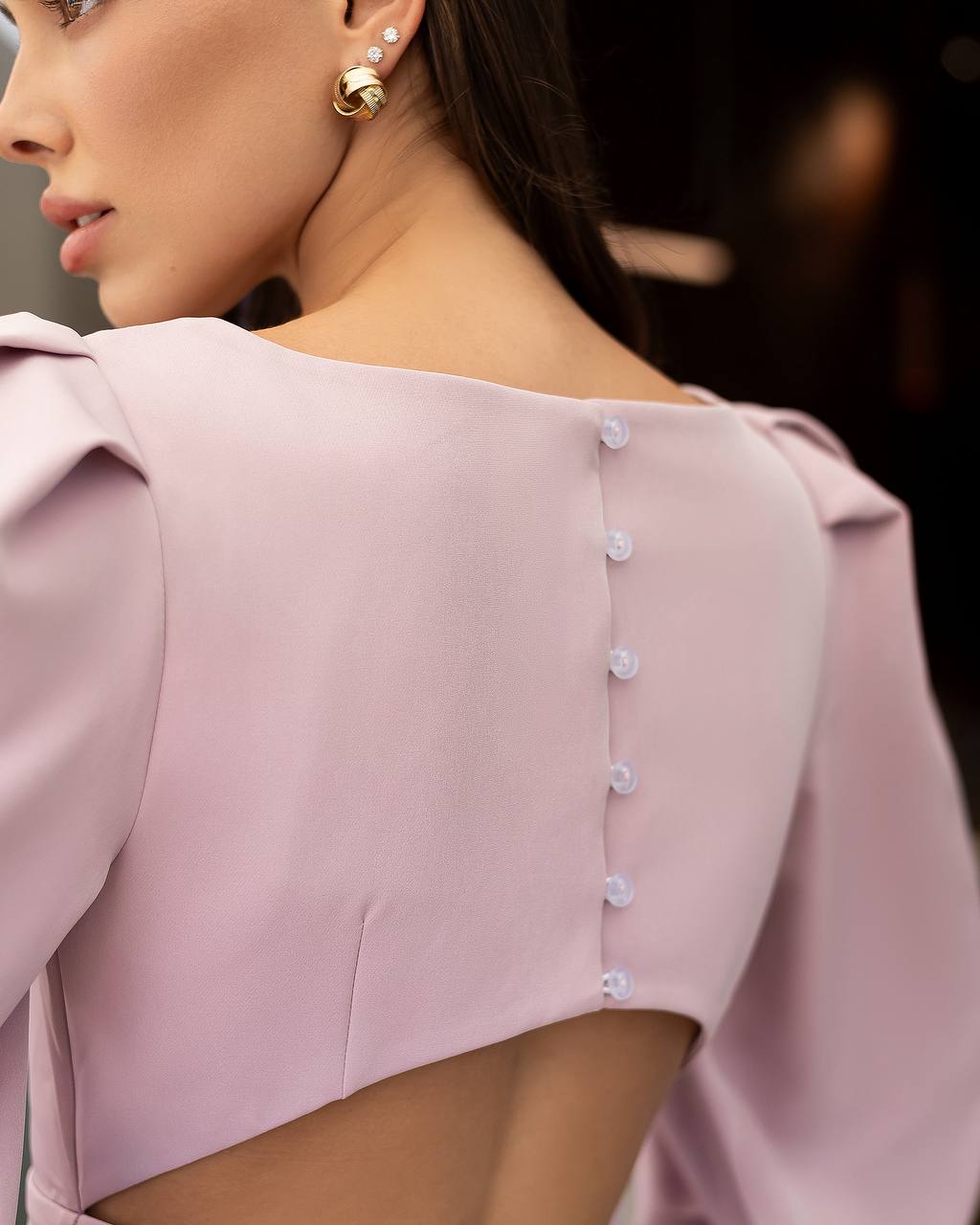 Close-up of a woman wearing a light pink blouse with button details.