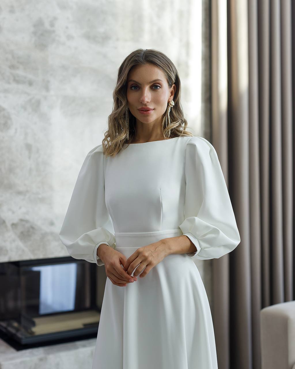 Woman wearing a white dress with puffed sleeves in an indoor setting.