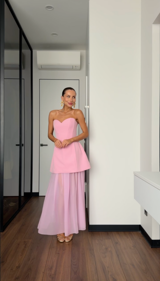 Woman in a pink strapless gown standing in a room with wooden flooring and white walls.