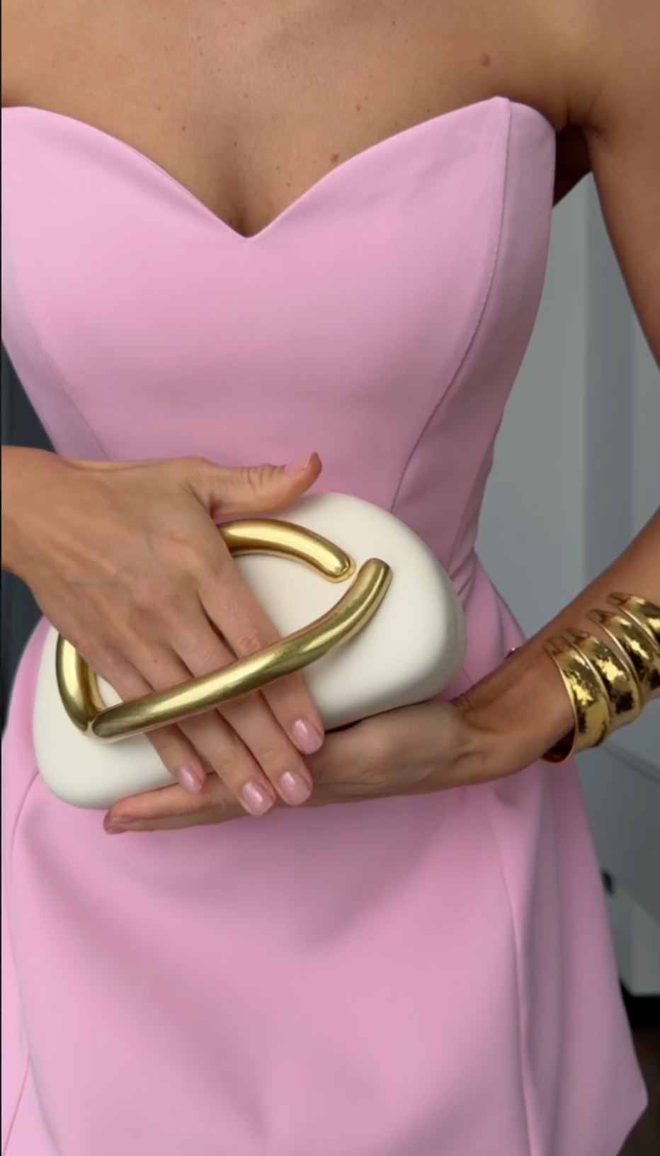 Person wearing a pink dress holding a white clutch with gold accents.