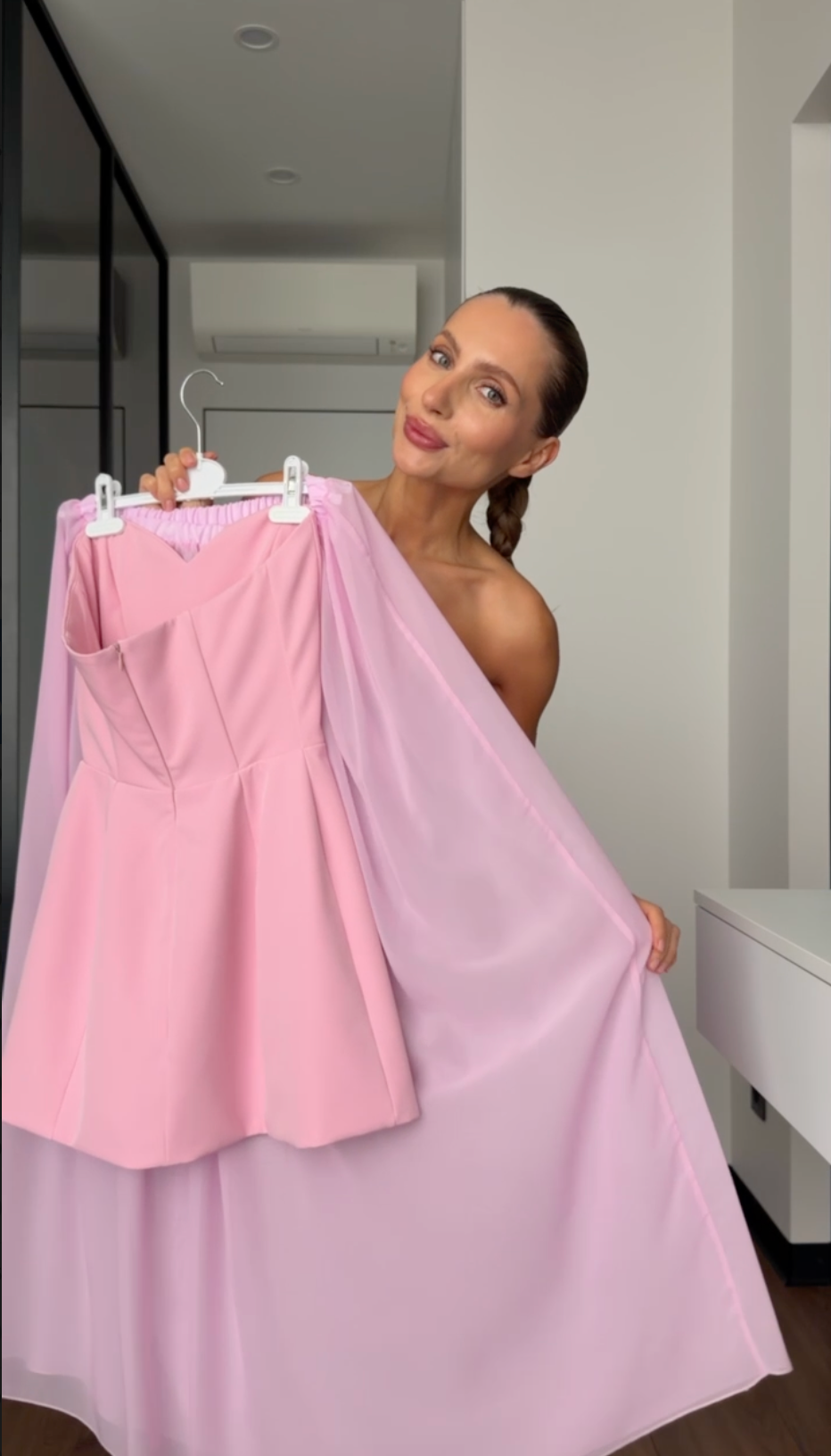 Woman holding a pink dress on a hanger in a room.