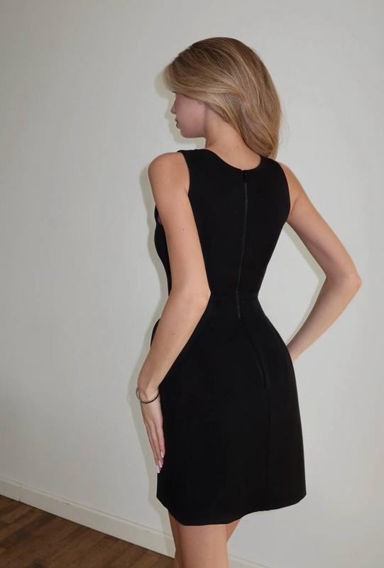 Woman wearing a black dress against a plain white wall