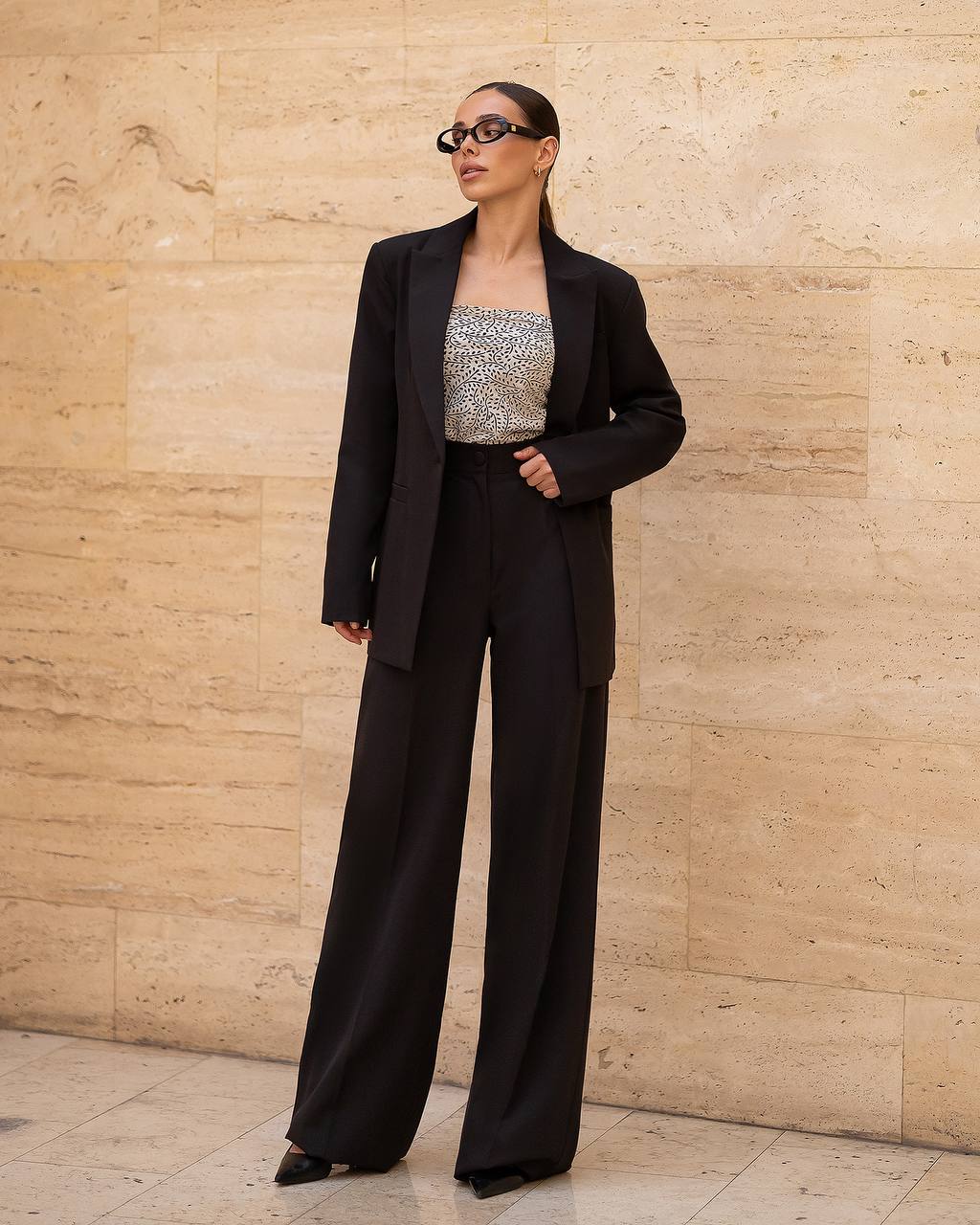 Person wearing a black suit and sequin top against a beige wall.