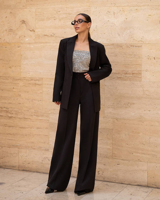 Person wearing a black suit and sequin top against a beige wall.