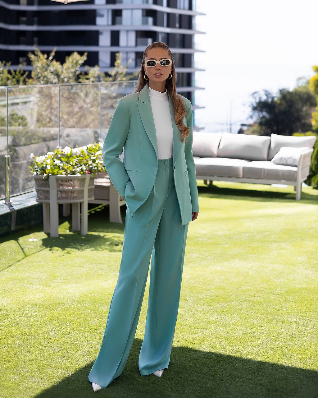 Woman in a teal suit standing on a grassy rooftop with modern buildings in the background