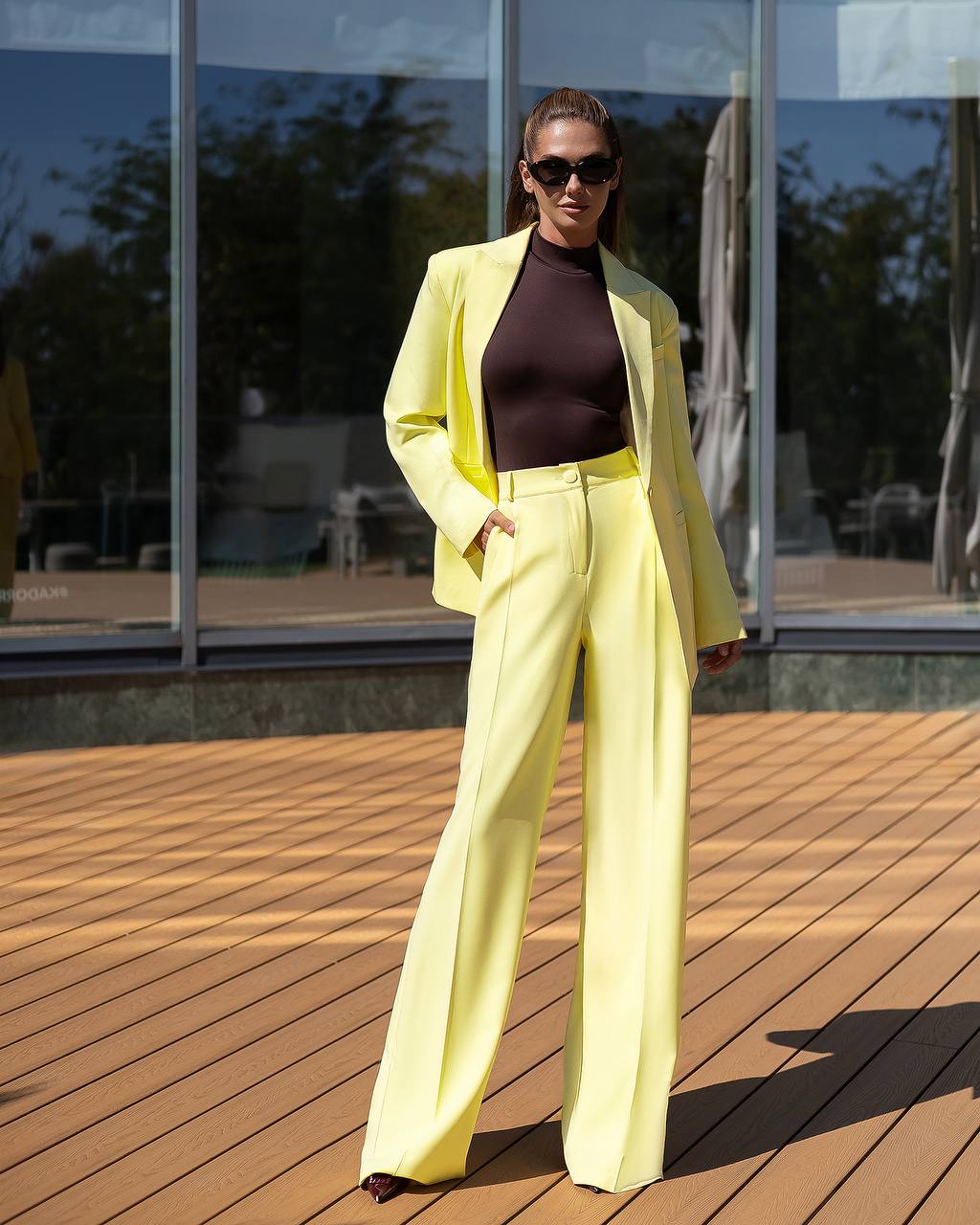 Woman in a bright yellow suit standing on a wooden deck.