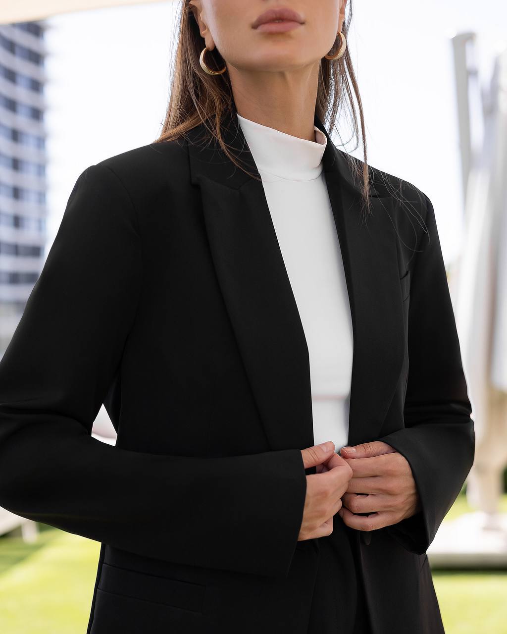 Person wearing a black blazer over a white shirt with a blurred outdoor background