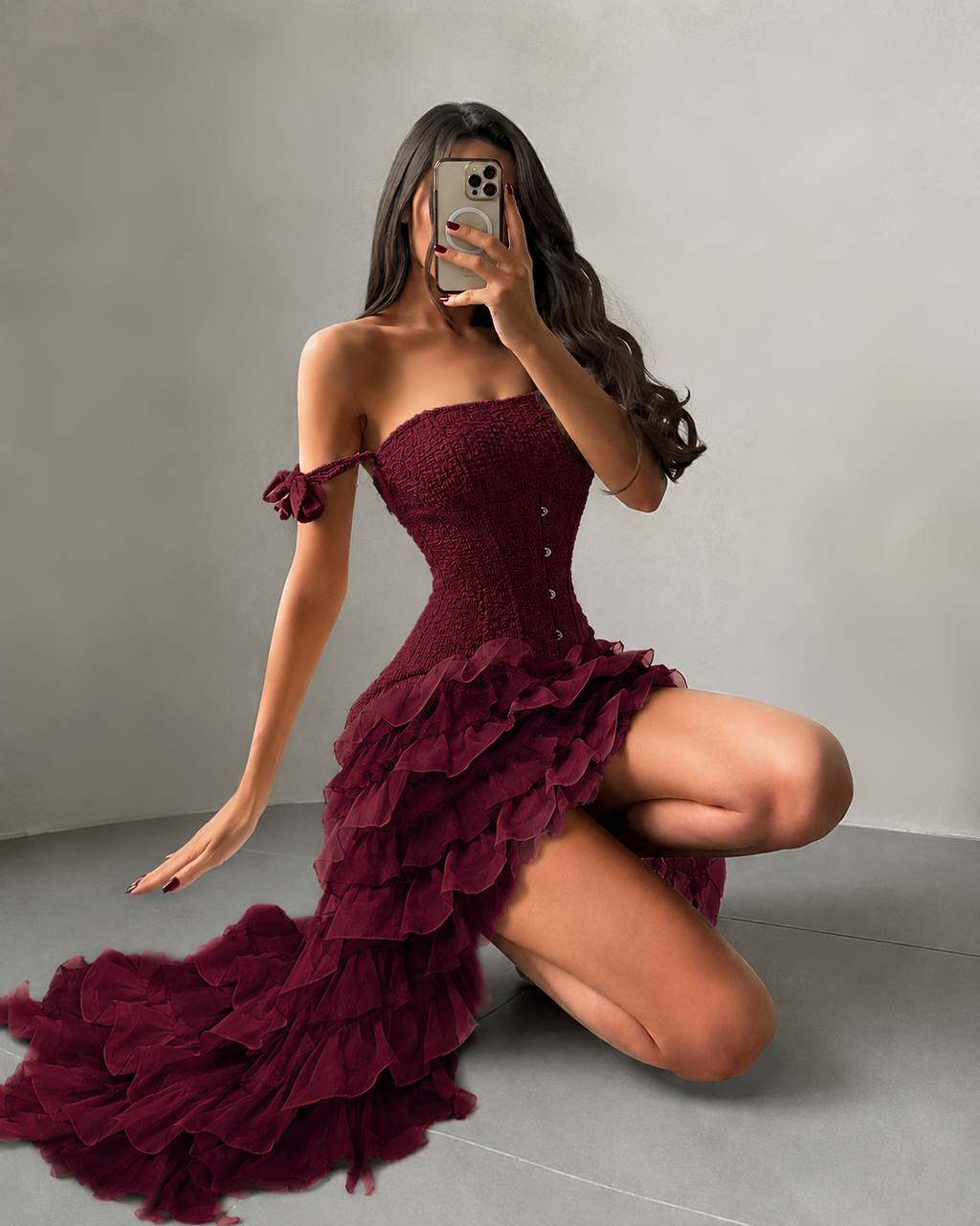 Woman wearing a burgundy off-shoulder dress posing against a plain background