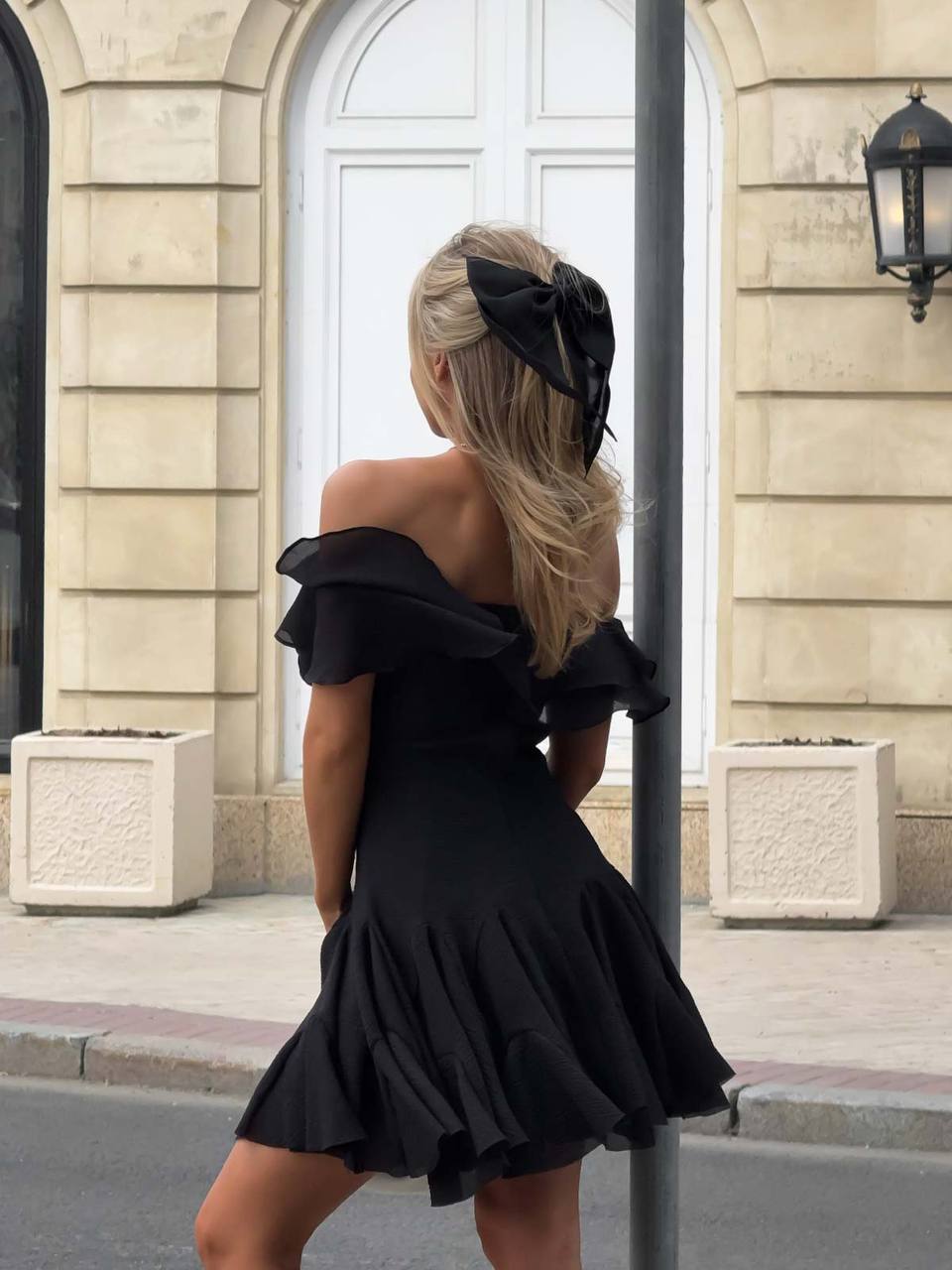 Woman in a black off-shoulder dress with ruffles walking on a street.