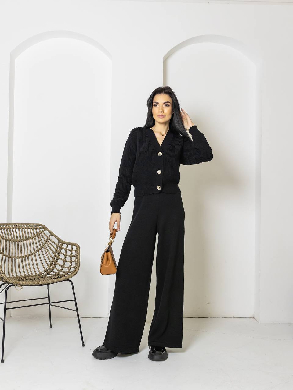Woman in a black outfit standing in a minimalistic room with a chair and arches.